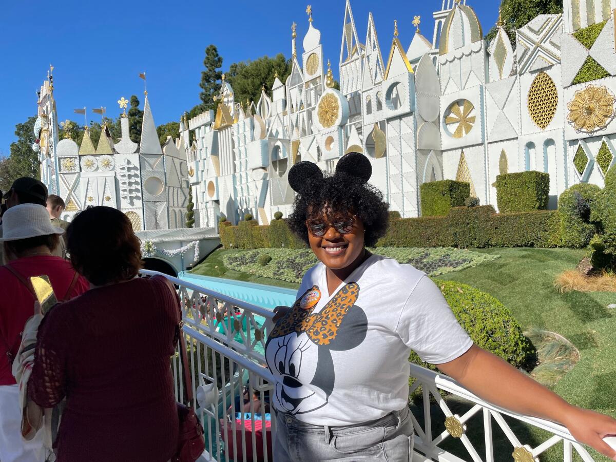 A woman wearing Mickey Mouse ears leans against a railing while posing for a photo