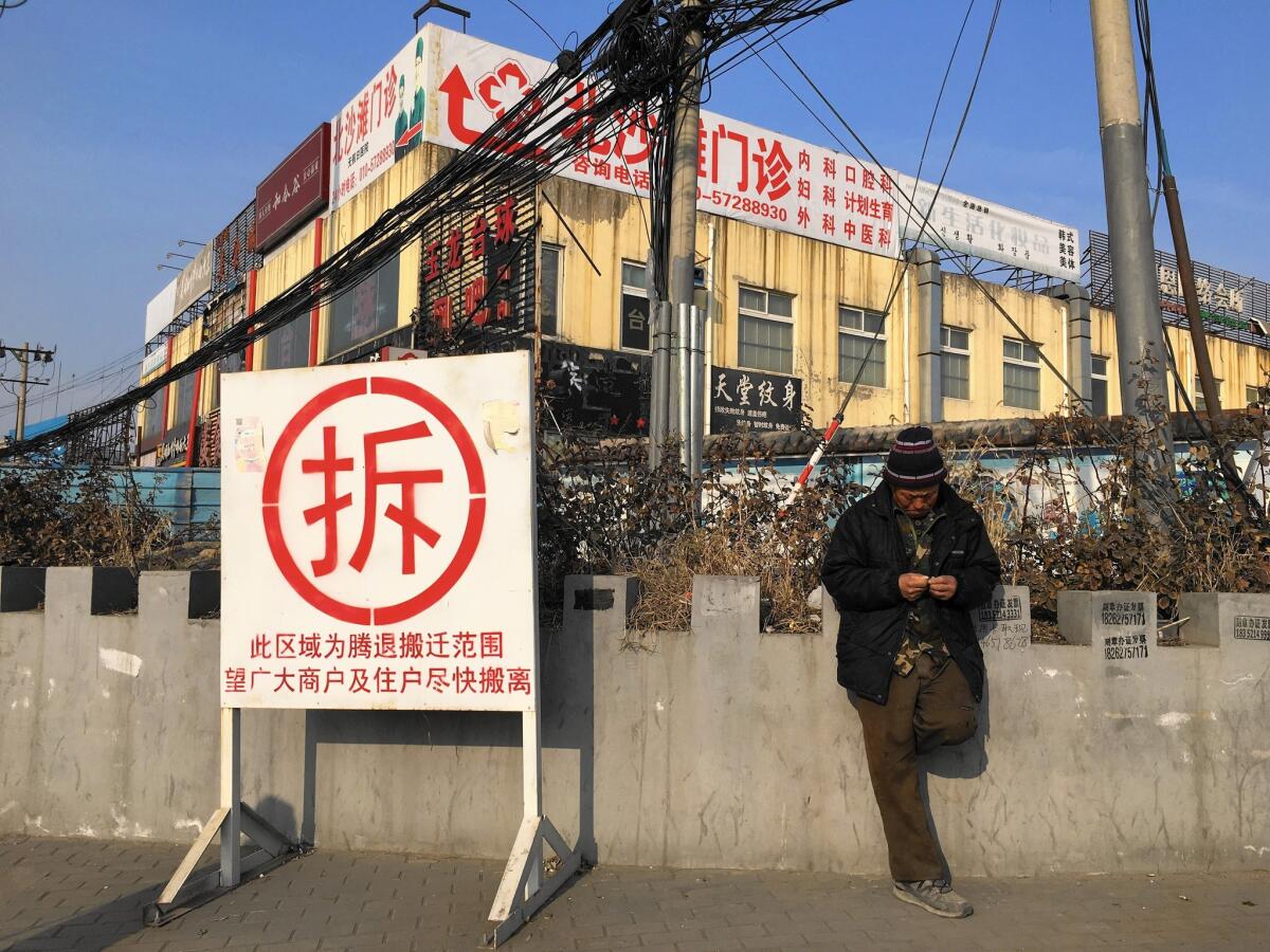 A man in Dongsheng, one of Beijing's largest slums, stands next to a sign reading "demolish." The area is set to be torn down this year, uprooting an estimated 100,000 people.