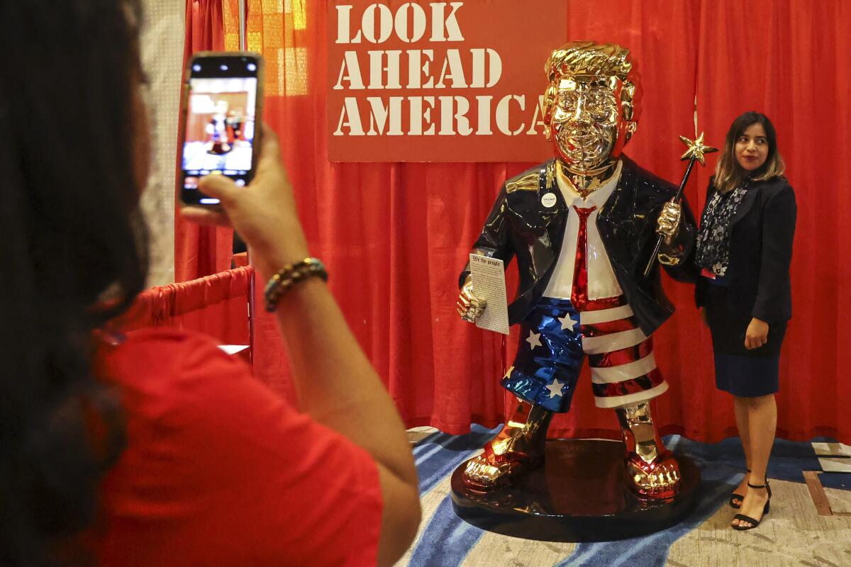 Una mujer se toma una foto junto a una estatua dorada de Donald Trump