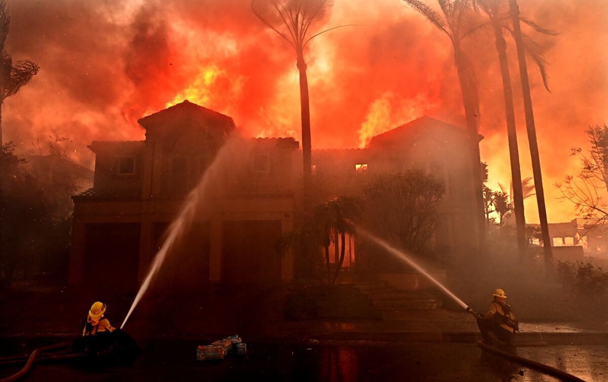 Firefighters aim water at a burning house