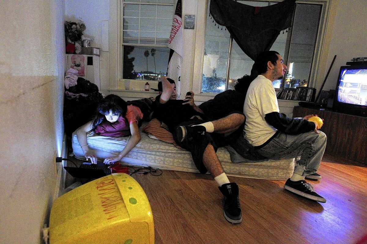 Sixteen-year-old Monica, left, plays solitaire on a laptop as her brothers Cesar and Jonathan watch TV in the tiny apartment they share with four additional family members. Stretches of Los Angeles and Orange counties have some of the most crowded housing in the country.