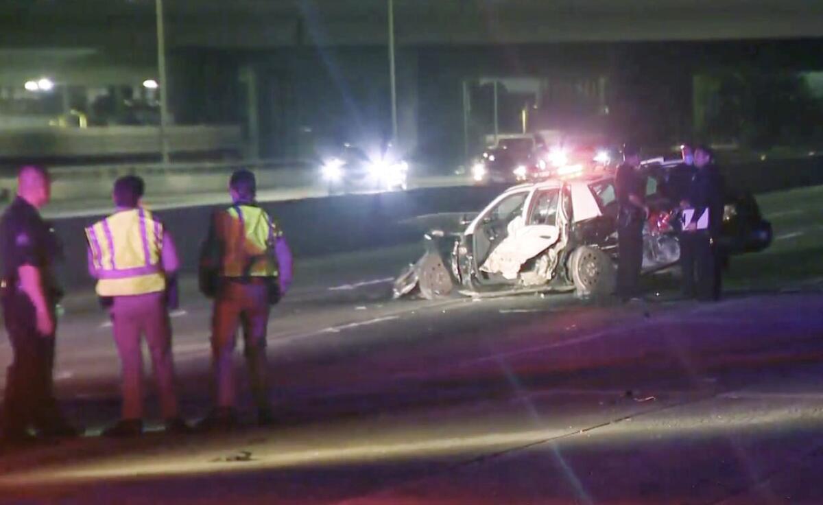 Officers stand near crashed police car on freeway.