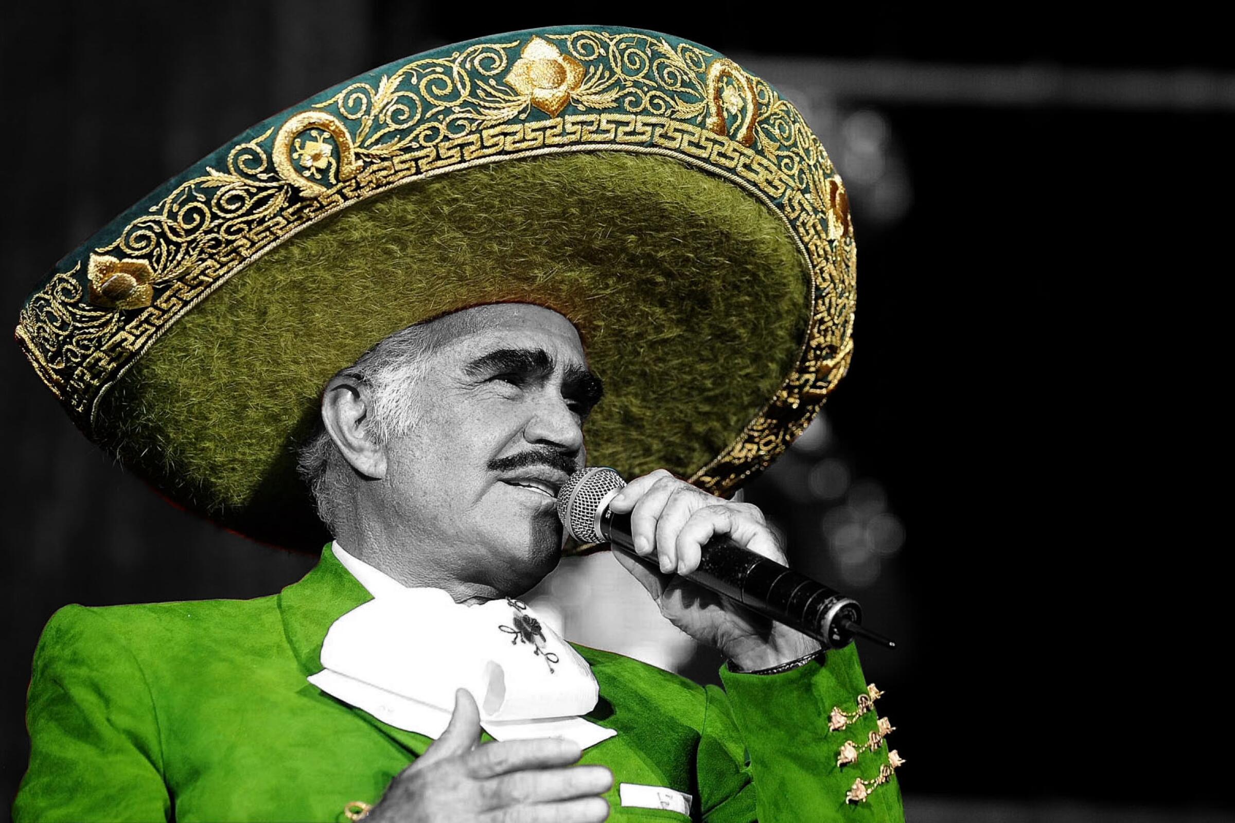 A mustachioed man in an elaborately embroidered sombrero and green jacket holds a microphone 