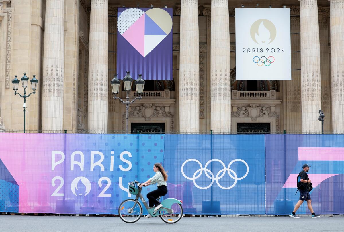 People ride and walk past the Grand Palais on Tuesday before the Olympics begin Paris.