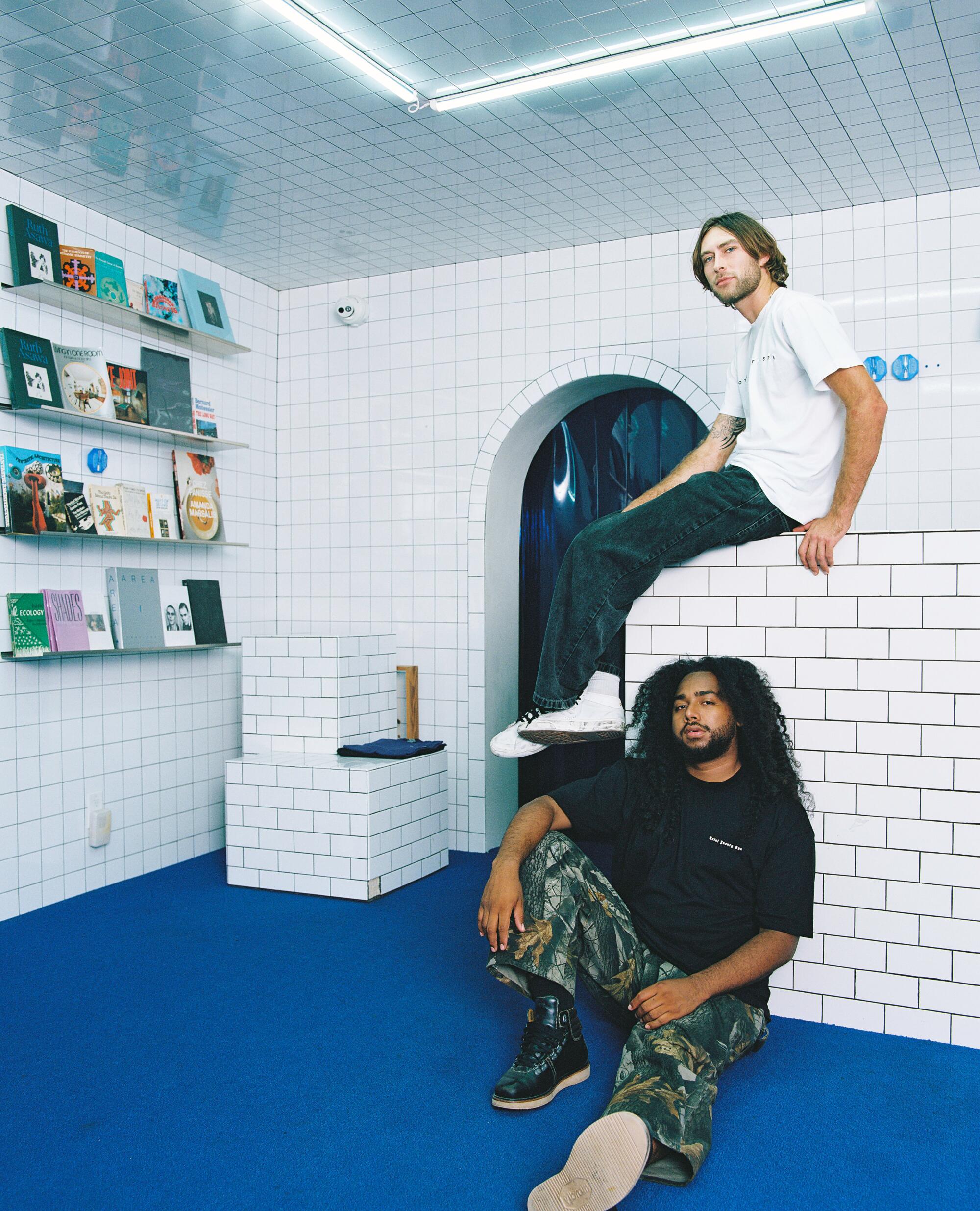 Two men sit inside a tiled store with blue floors.