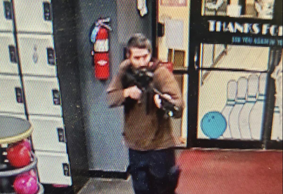 A still from a video taken from above of a man aiming an assault-style rifle inside a bowling alley