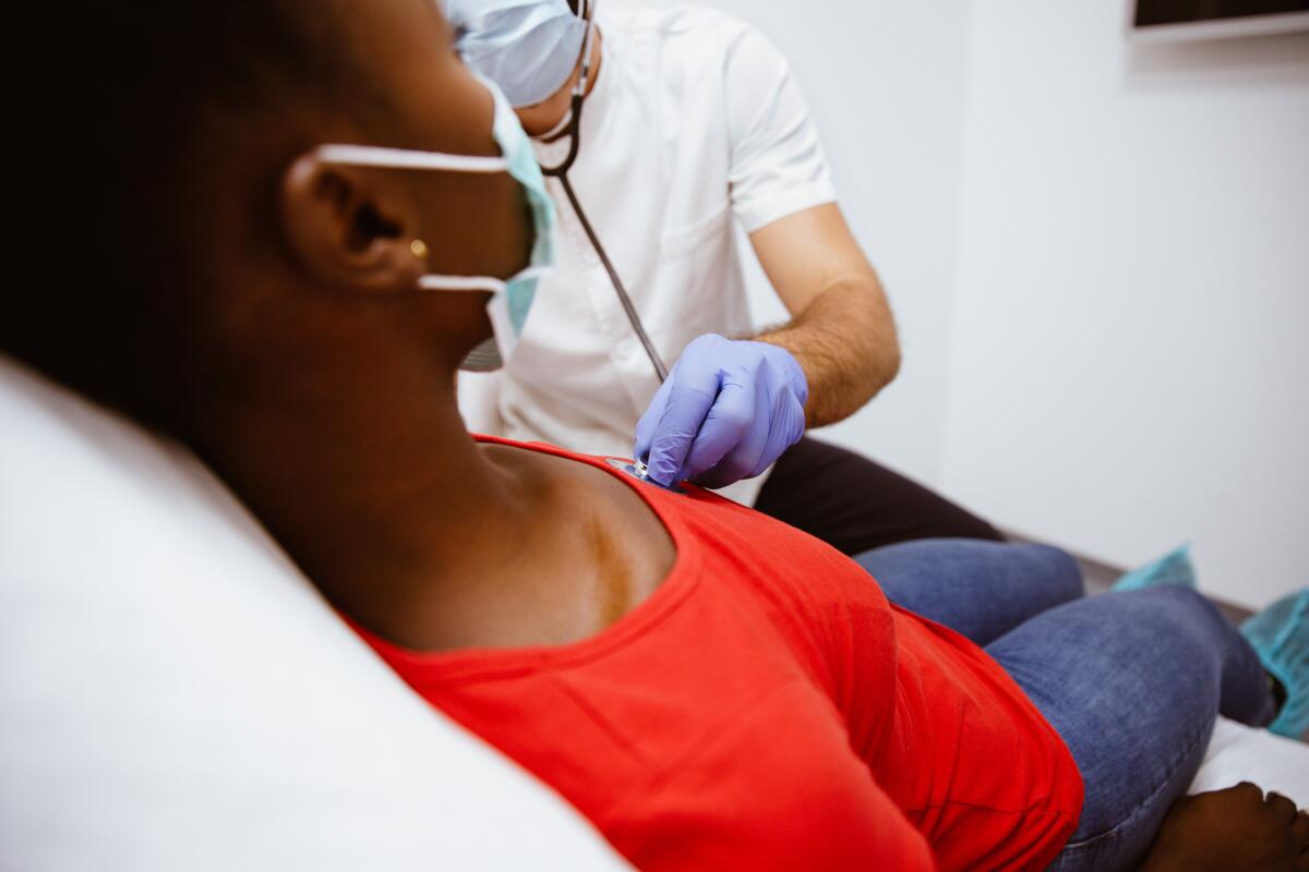 A healthcare worker uses a stethoscope to listen to a young person's heart.