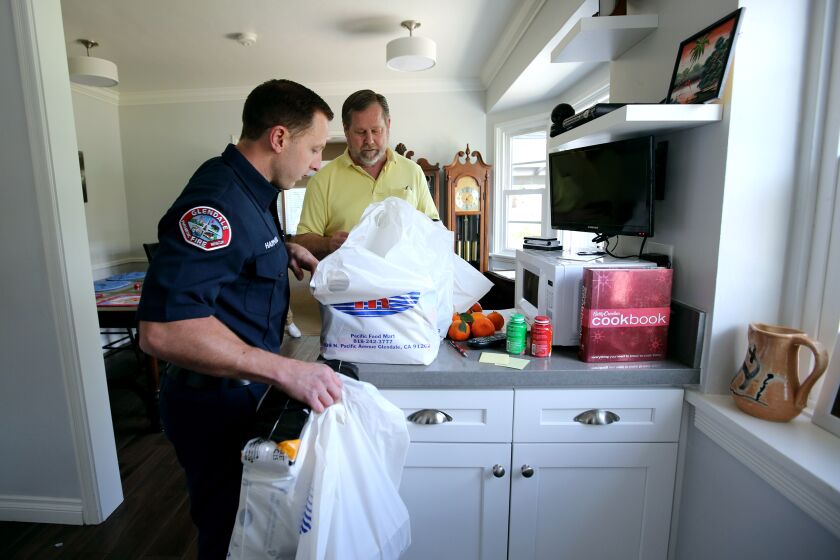 Glendale Fire Dept. firefighter paramedic Spencer Hammond, left, volunteered to shop for and deliver critical food items to the home of 64-yr. old Jim Rohrig, who has respiratory issues, in Glendale on Wednesday, March 18, 2020. Rohrig, who's 74-yr. old wife suffered a stroke, can't leave his home much, he paid for the food in cash according to the receipt from the store and without any additional service or delivery fees. Rohrig will share the food Hammond brought with an elderly tenant and an elderly next-door neighbor.