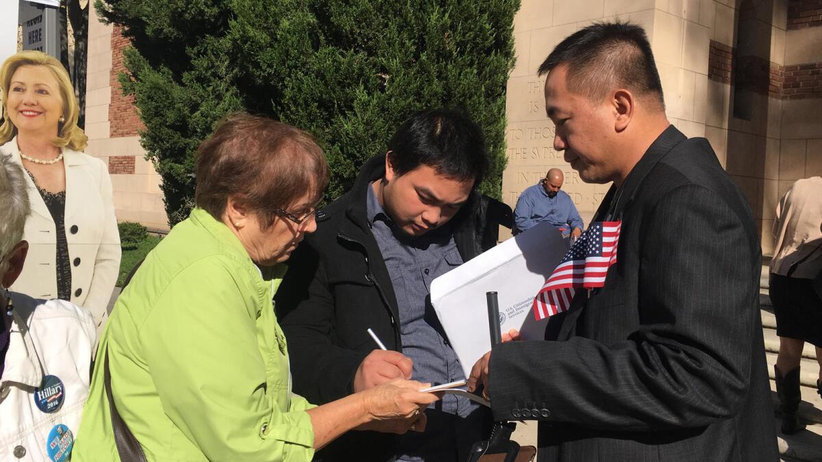 Thomas Macariola, center, fills out a voter registration form after a naturalization ceremony on Oct. 26 in Sacramento, where a cardboard cut-out of Democratic presidential candidate Hillary Clinton was among the witnesses.