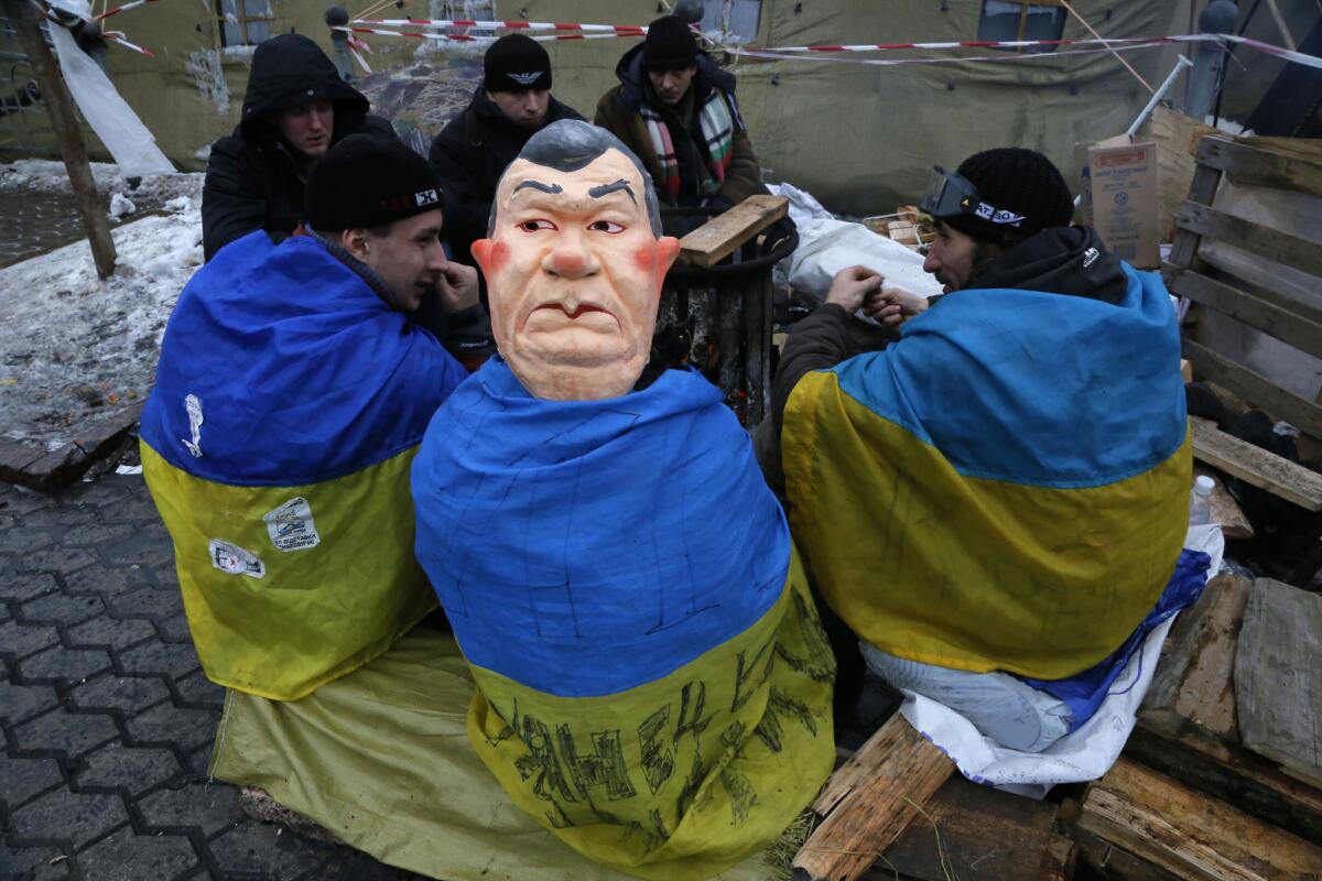 A pro-European Union activist wearing a mask depicting Ukrainian President Viktor Yanukovich sits with others as they warm themselves near a bonfire in Independence Square in Kiev, Ukraine.