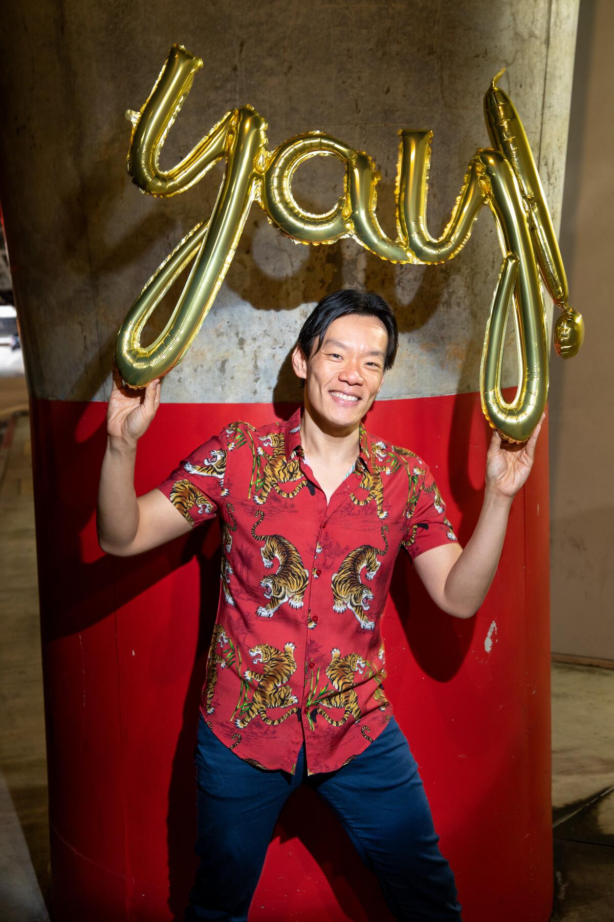 Man with red shirt holding  balloon spelling the word "Yay"