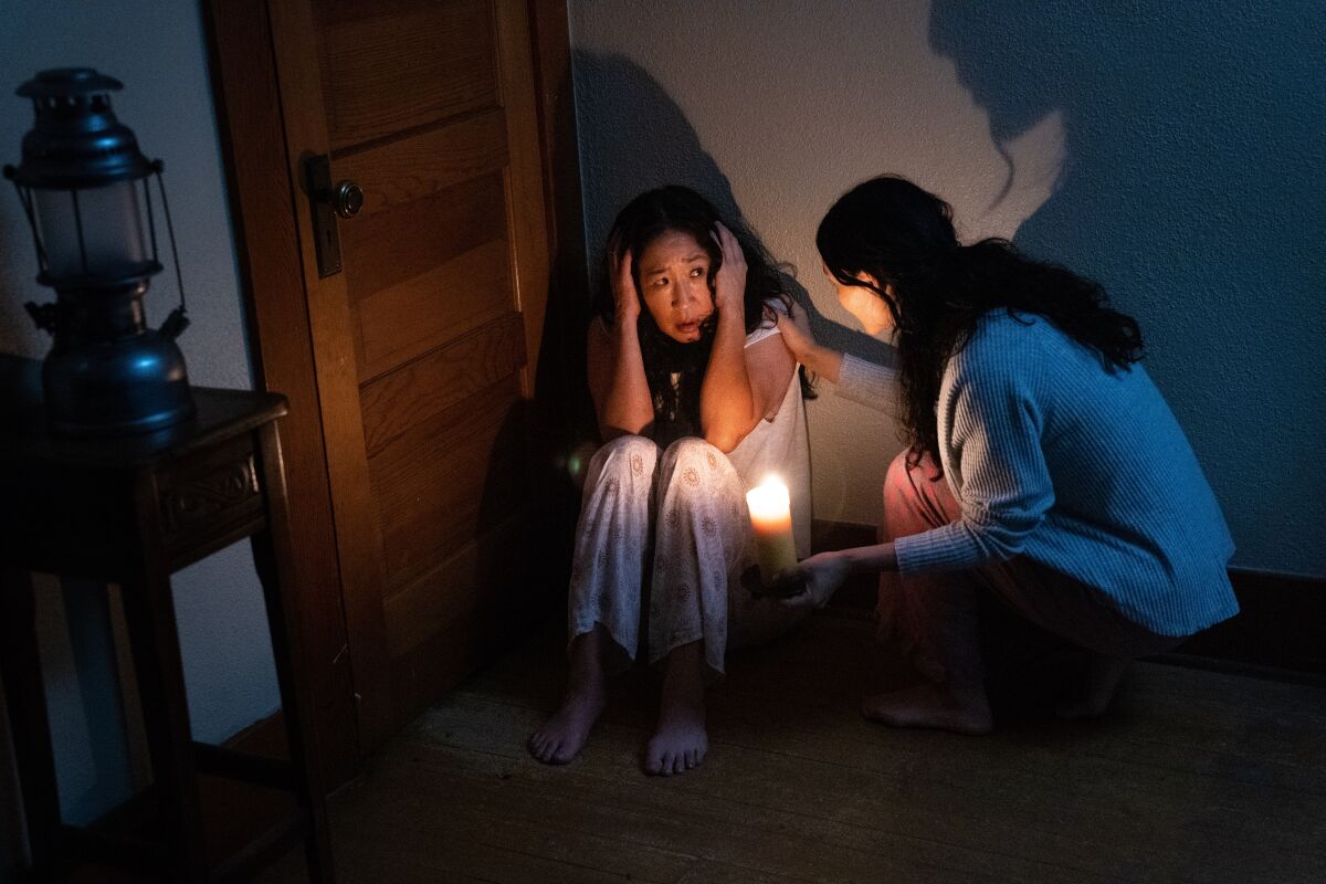 A woman holding a candle checking on a woman crouched on the floor