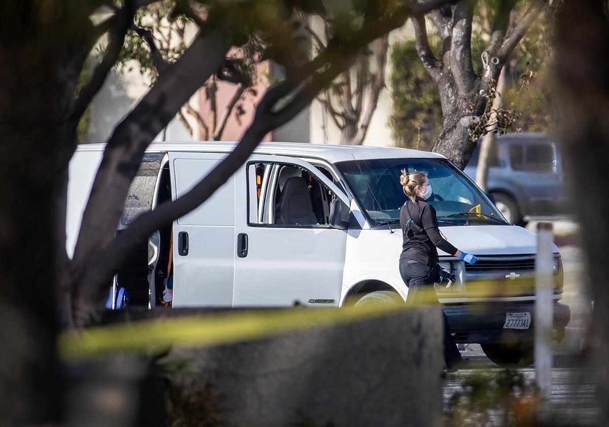 A person in a mask walks near a white van with its doors open and a window broken in a parking lot.