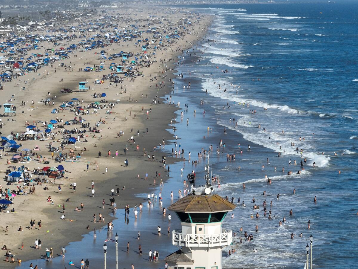 In an aerial view of a large crowd of people on the beach and in the surf waters
