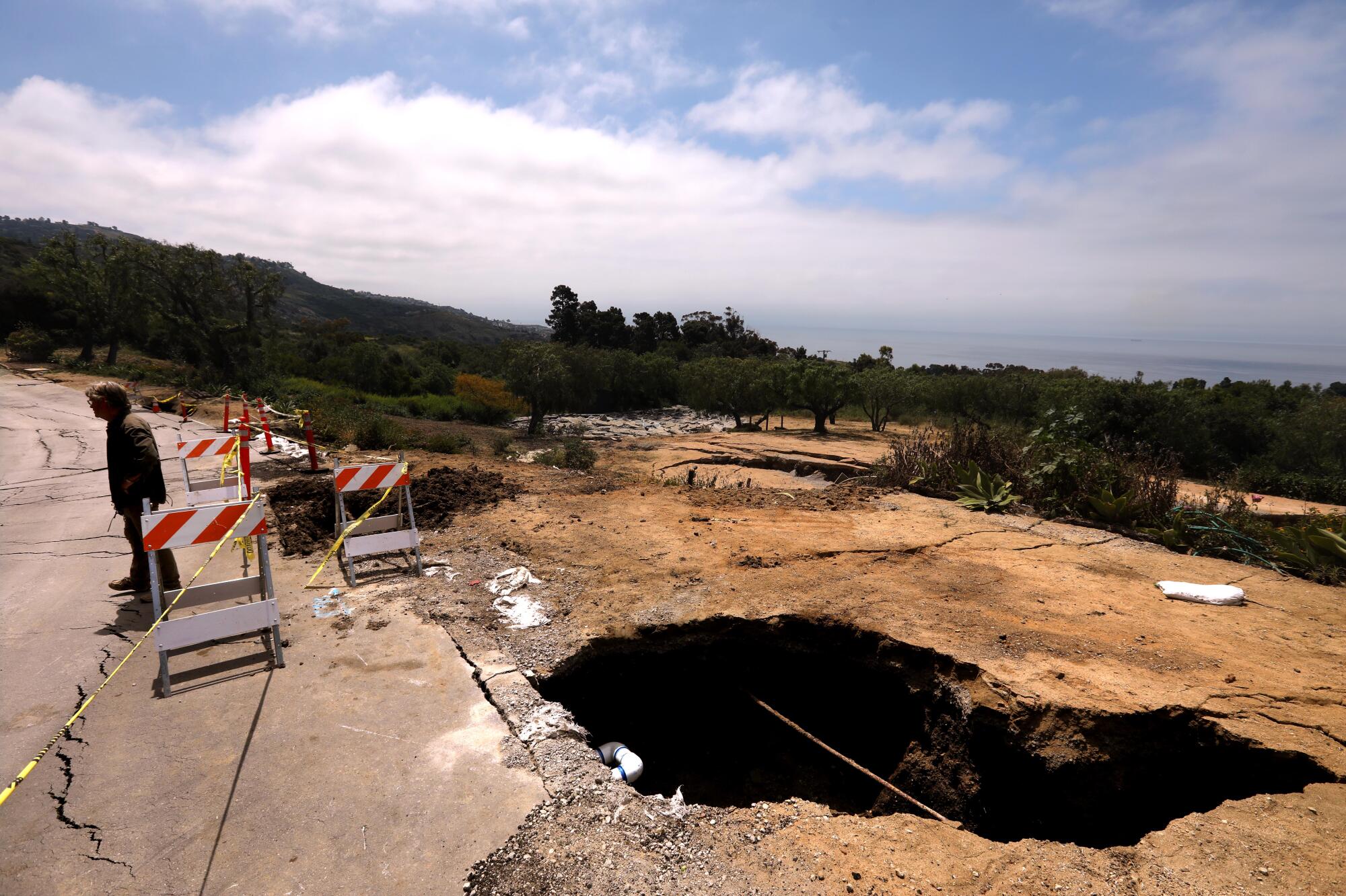 A man stands near a gaping hole in bare earth.