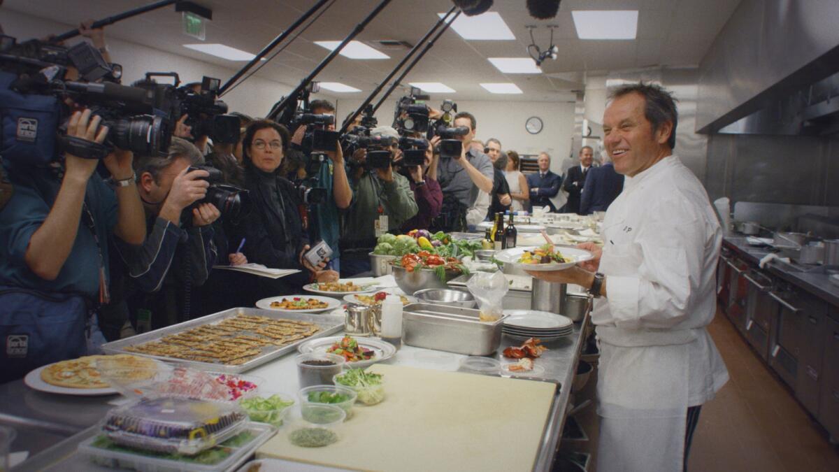 A chef stands in his kitchen facing camerapeople and reporters in the documentary "Wolfgang."