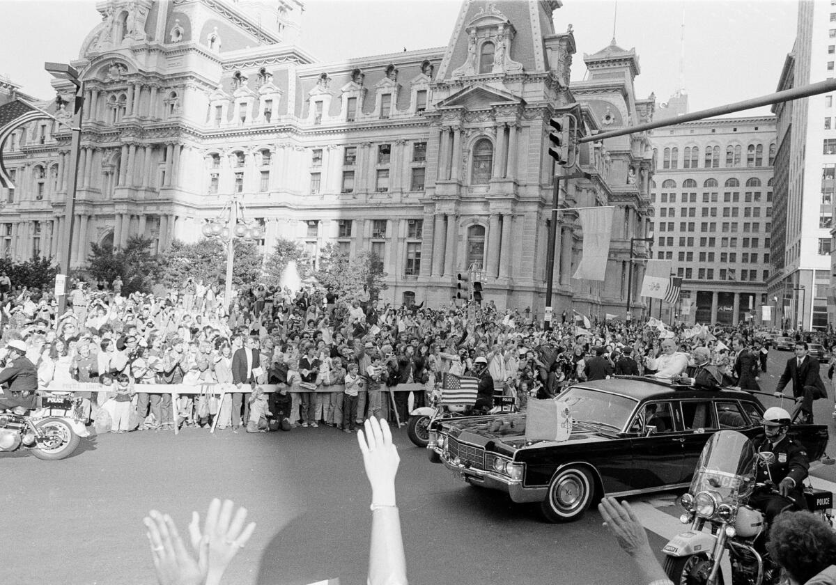 Pope John Paul II, in white, and Cardinal John Krol wave to the welcoming crowd as their motorcade passes City Hall in downtown Philadelphia, Pa., Oct. 3, 1979.