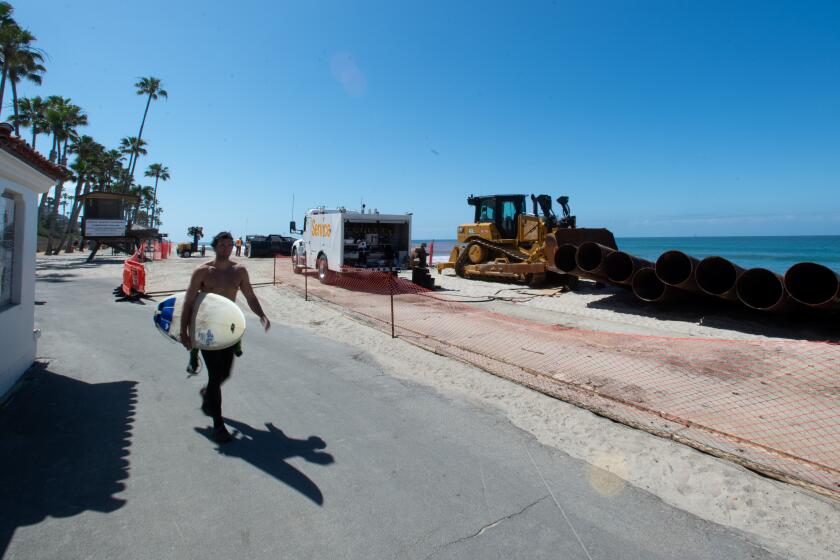 A surfer walks past a fenced off construction zone in San Clemente where crews will soon begin working on a beach nourishment project