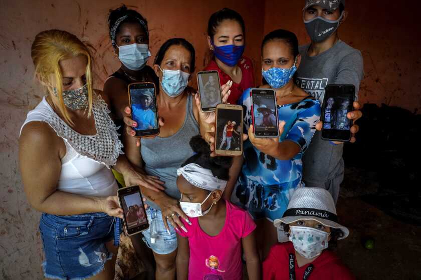 Zuleydis "Zuly" Elledias, left, shows a cellphone photo of her missing husband to a child while her neighbors pose for a group picture holding up cellphone photos of their missing relatives who ventured out in homemade boats in an attempt to reach Florida, in Orlando Nodarse, about 60 kilometers west of Havana, Cuba, Wednesday, June 30, 2021. Cuba is seeing a surge in unauthorized migration to the United States, fueled by an economic crisis. (AP Photo/Ramon Espinosa)