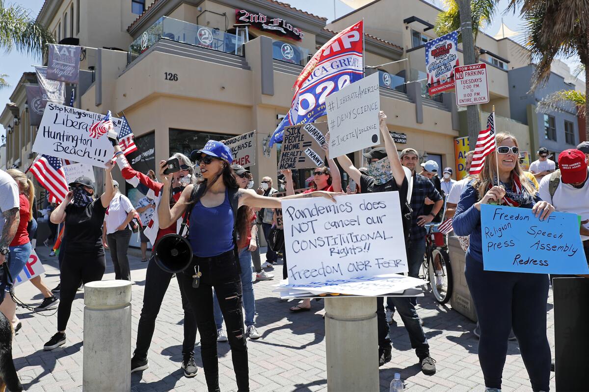 Protesters hold signs and wave flags at the intersection of Main Street and Walnut Avenue in downtown Huntington Beach on Friday.