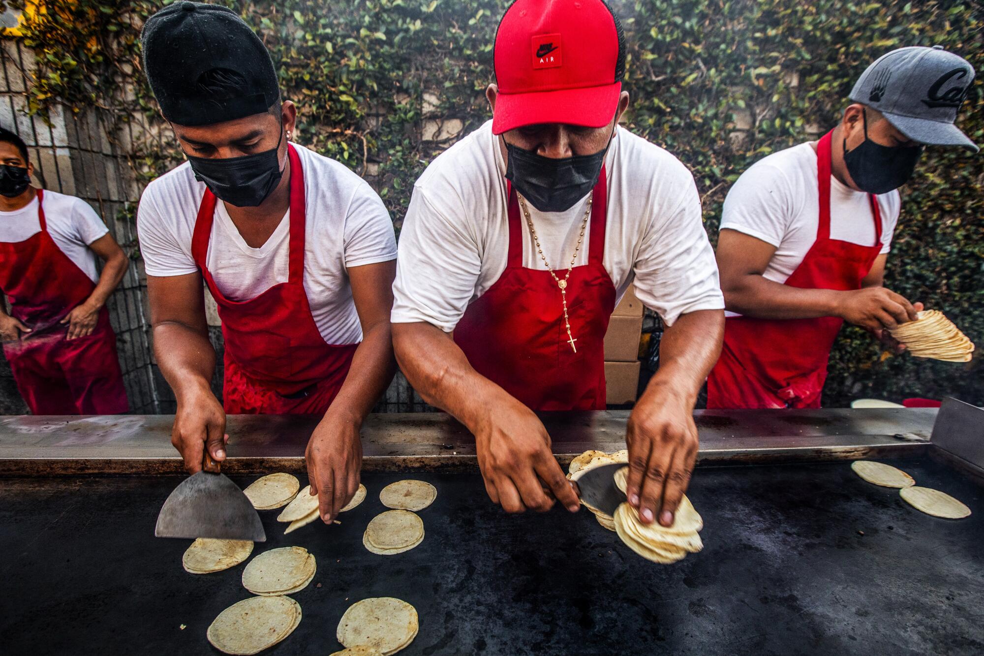 Cooks handle tortillas on and near a flat-top grill.