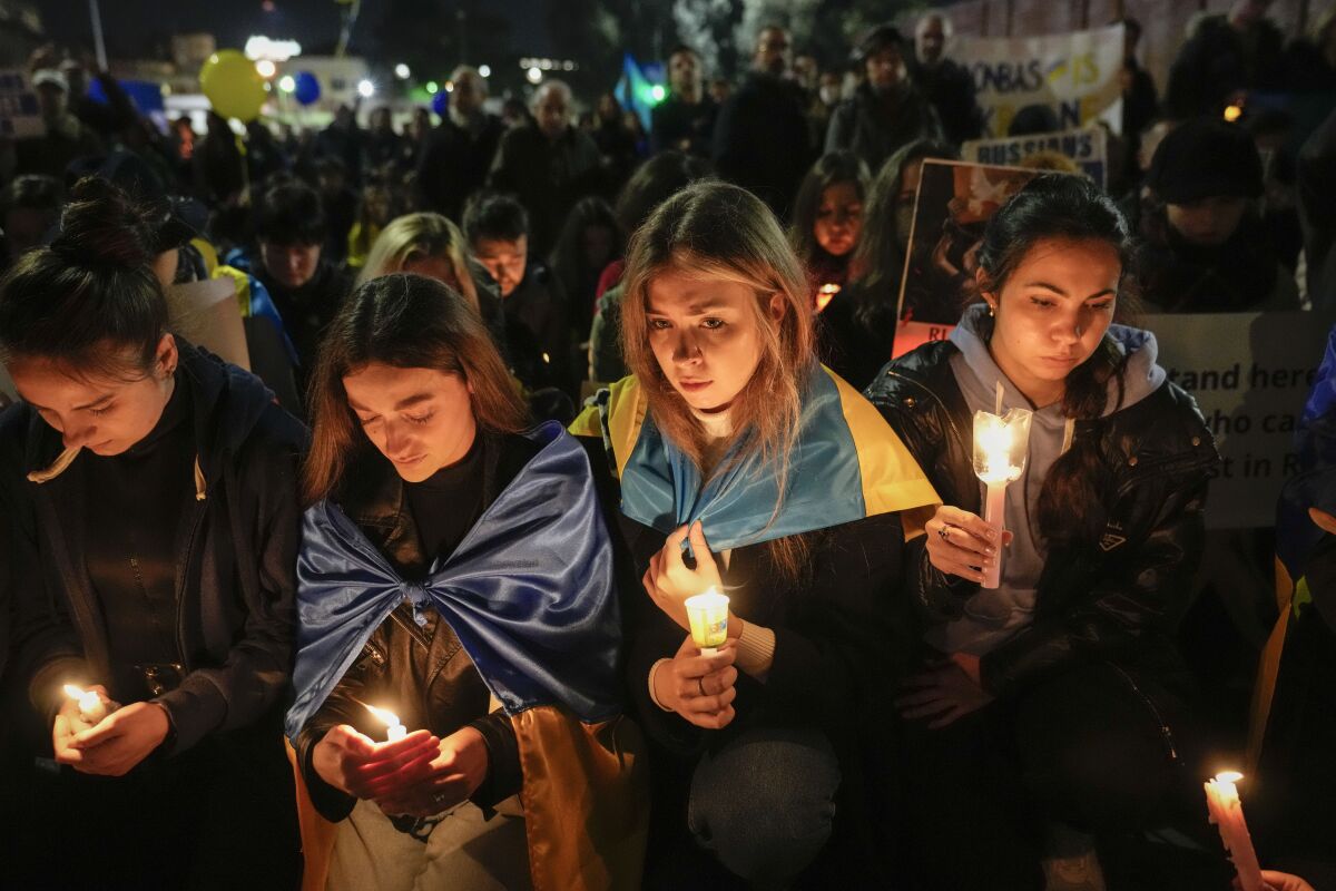 Women holding candles in the dark as people in the crowd behind them hold signs and blue and yellow balloons
