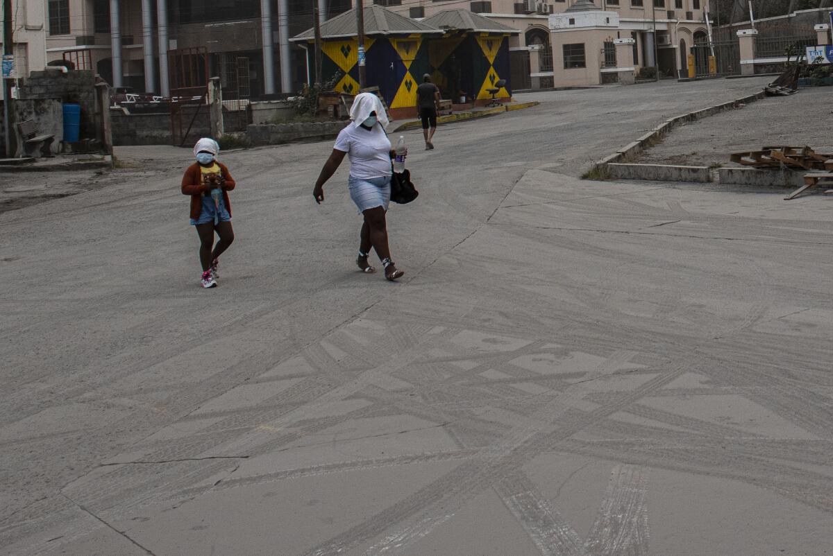 A woman and a girl wearing protective head coverings walk on a street covered with volcanic ash.