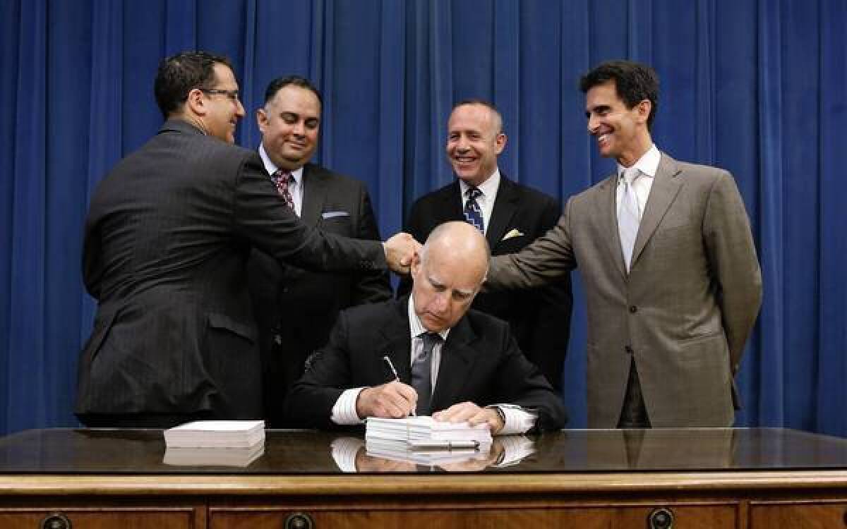 Gov. Jerry Brown signs the state budget on Thursday as Assembly Budget Chairman Bob Blumenfield (D-Woodland Hills) and Senate Budget Chairman Mark Leno (D-San Francisco) shake hands.
