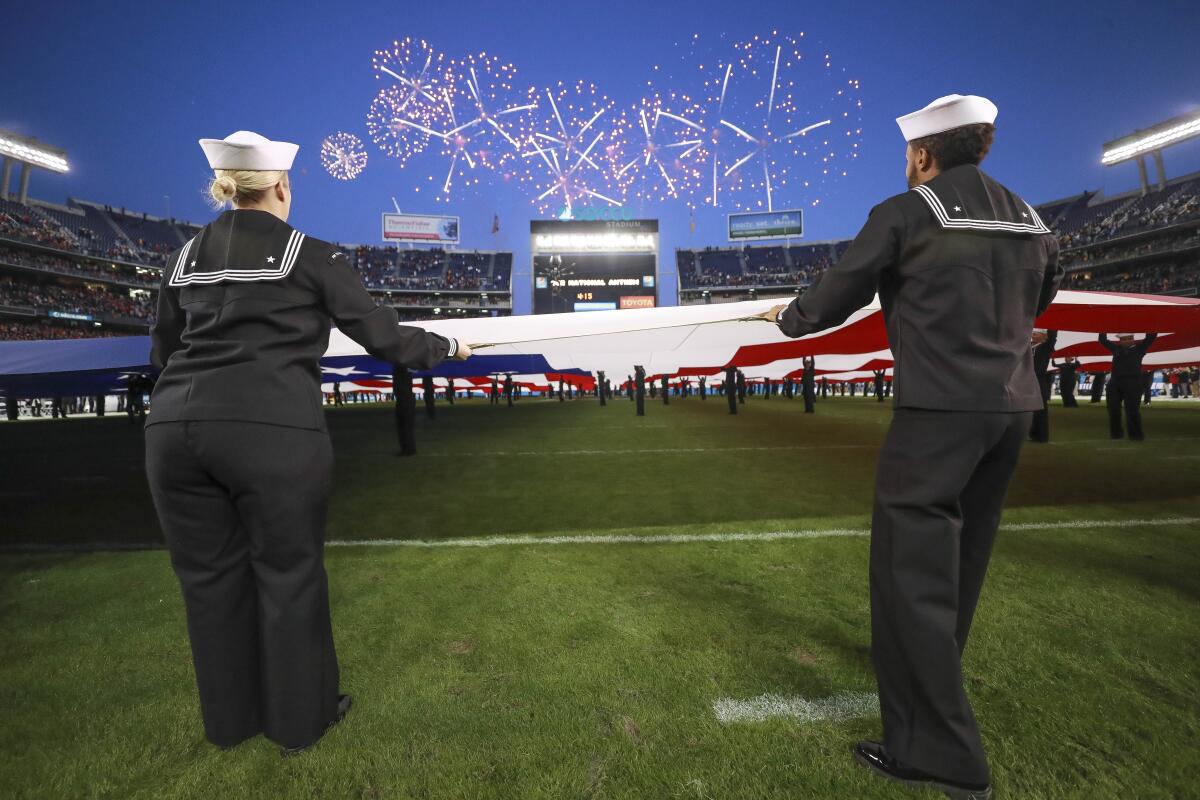 Members of the military holding a U.S. flag on a football field under fireworks