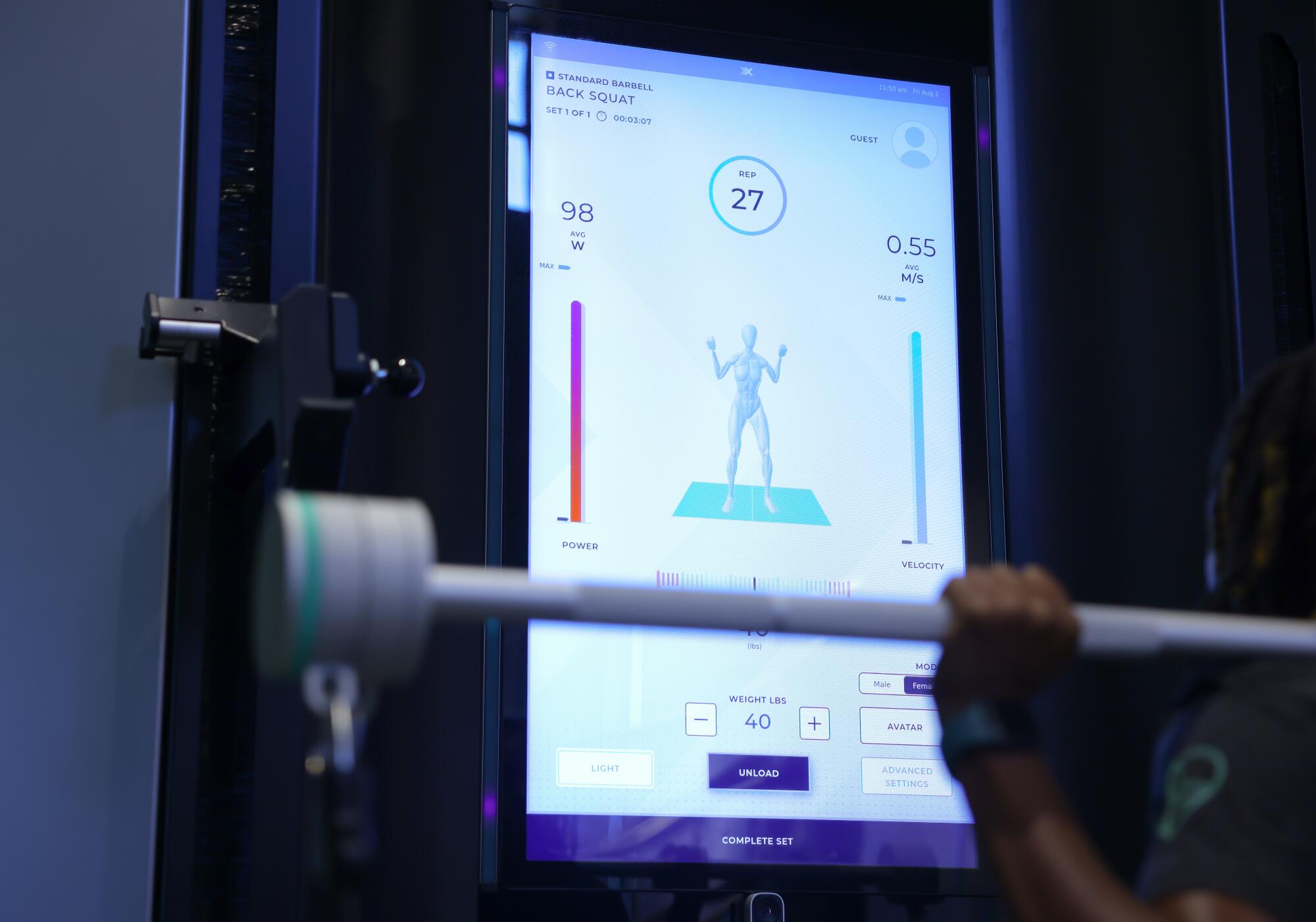 The screen of a high-tech OxeFit machine has a digital avatar for a person doing squats.