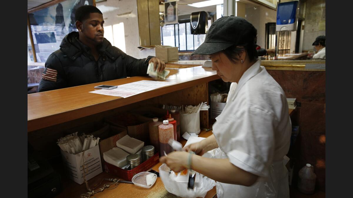 A cashier at China Doll Chinese Restaurant in Brooklyn, near the Pink Houses, gives change back to a customer.