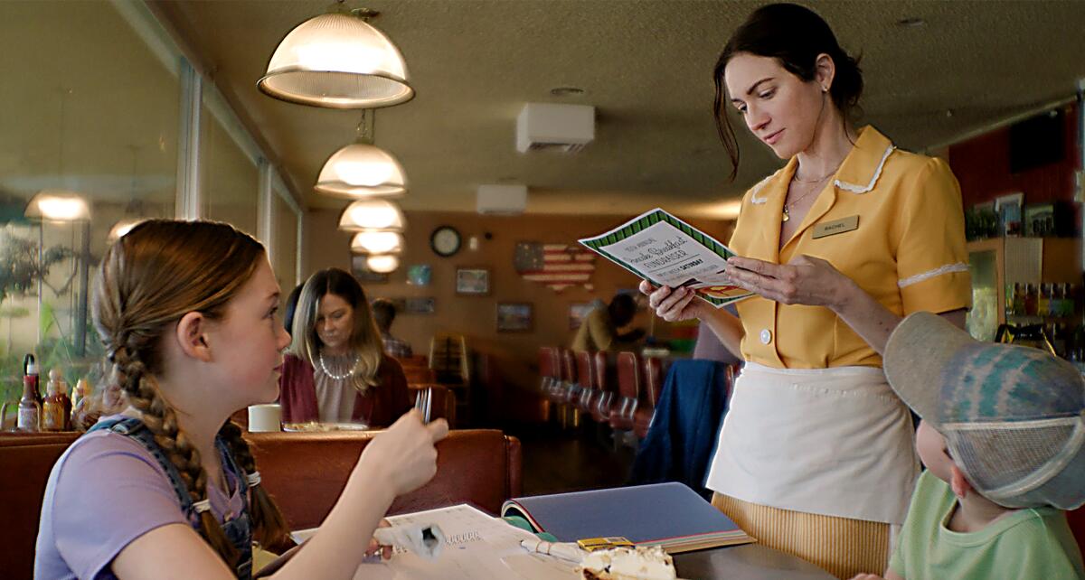 一位年轻女子和一个孩子坐在餐桌旁，看着他们的女服务员 