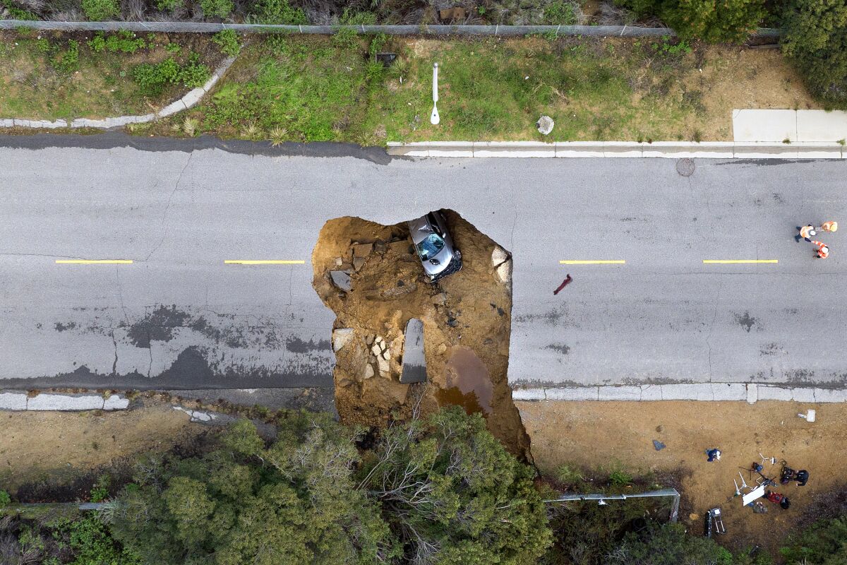 An aerial view of a horizontal road with a large sink hole in the middle and a car inside it.