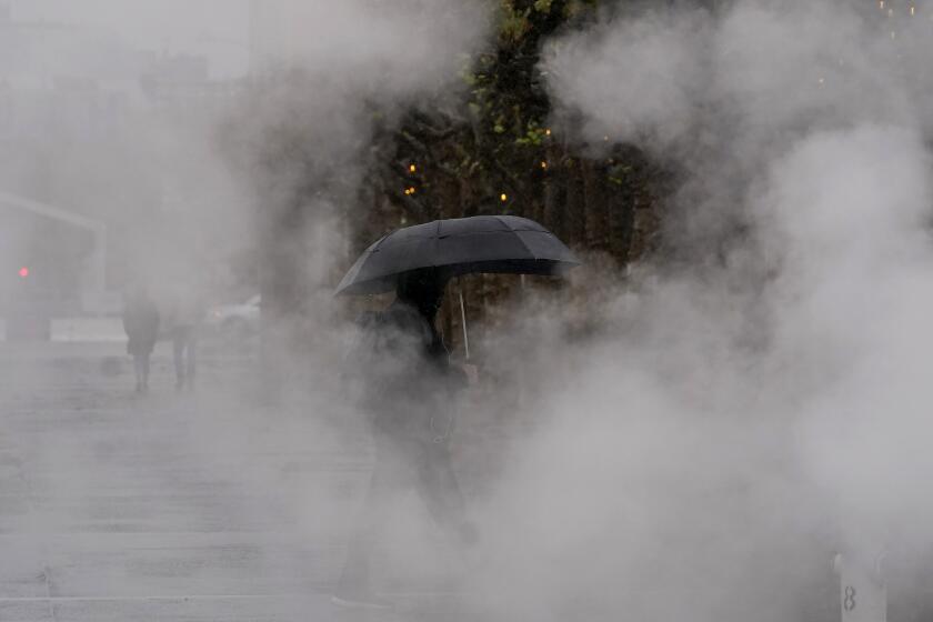 A pedestrian carries an umbrella while walking at Civic Center Plaza in San Francisco, Tuesday, Nov. 8, 2022. A major winter storm pounded California on Tuesday, bringing rain and snow to the drought-stricken state along with possible flash flooding in areas recently scarred by wildfires, meteorologists said. (AP Photo/Jeff Chiu)