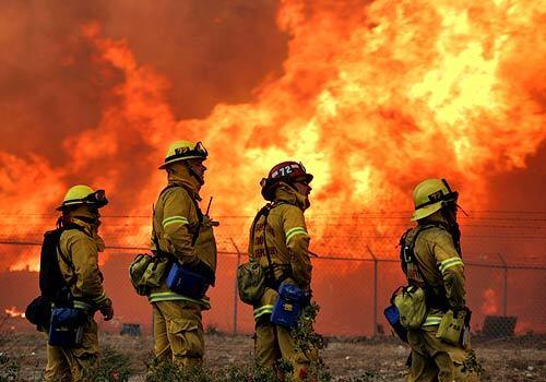 A wind-driven wildfire burned 200 acres of brush, torching an industrial yard where stacks of pallets exploded in flames, threatening as many as 100 homes.