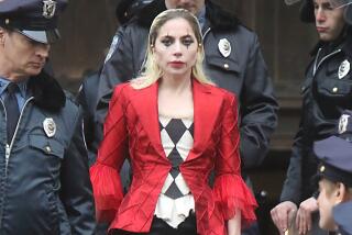 Lady Gaga wearing a red blazer, black-and-white blouse and clown makeup, surrounded by men in police uniforms