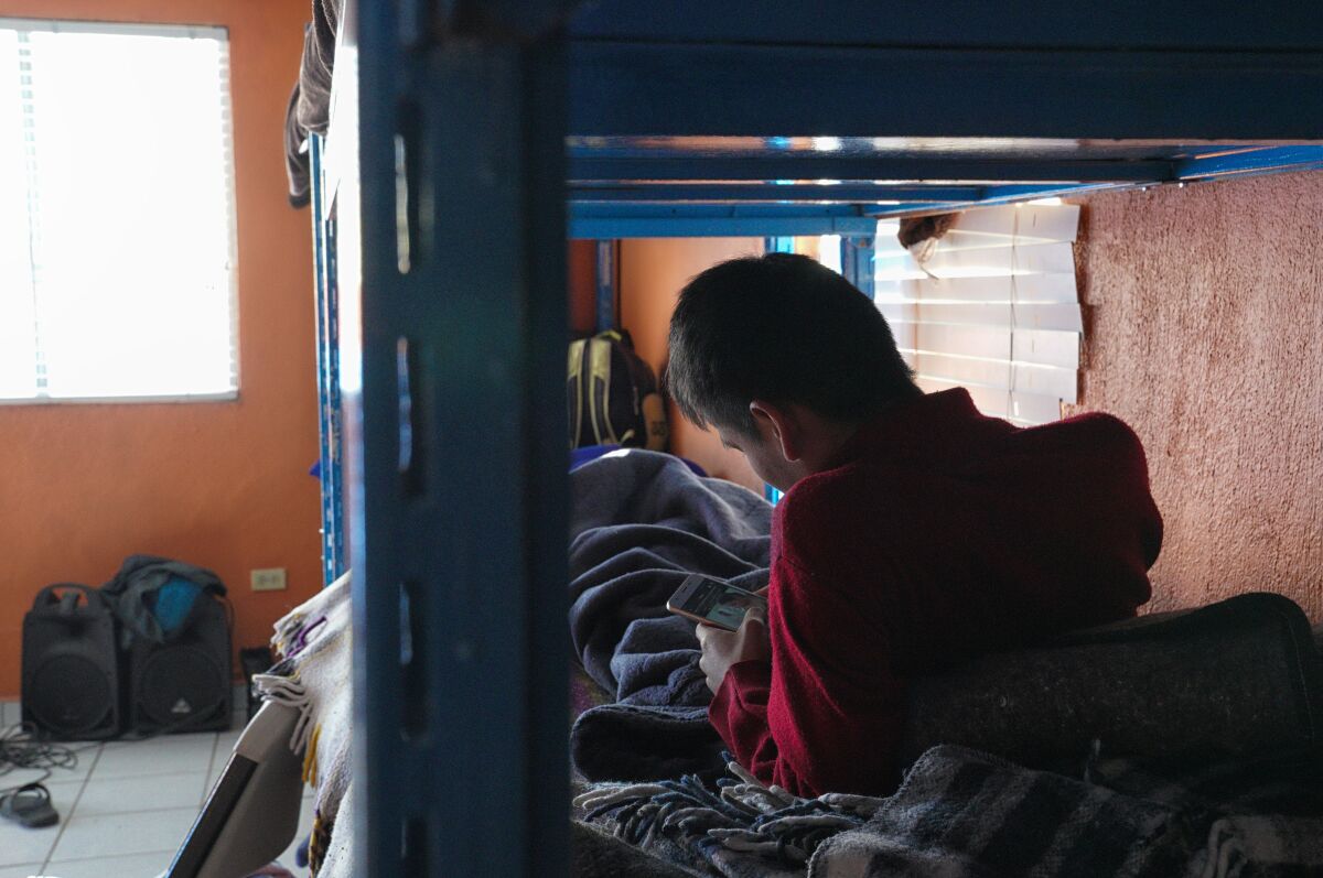 A boy lies on a bunk bed looking at his phone