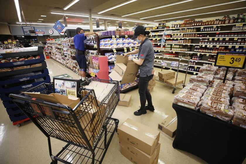 TORRANCE, CA - APRIL 27: Ping Moyer, right, working for Vons alongside Michael Mason who works for Orowheat as they stock shelves at the Vons located at 24325 Crenshaw Blvd in Torrance before doors open at 6 a.m. for seniors and at-risk shoppers due to the Coronavirus. Most of the team arrives at 5 a.m. to stock the shelves with product, sanitize the location for staff and shoppers, and picker/shoppers begin to collect items for .com home delivery shoppers. Vendors arriving throughout the morning must read a checklist of warnings, sign in and they must wear face covering. Vons on Monday, April 27, 2020 in Torrance, CA. (Al Seib / Los Angeles Times)
