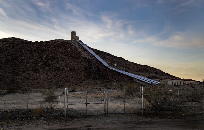 Water pipes run down a hillside at a facility behind chain-link fencing