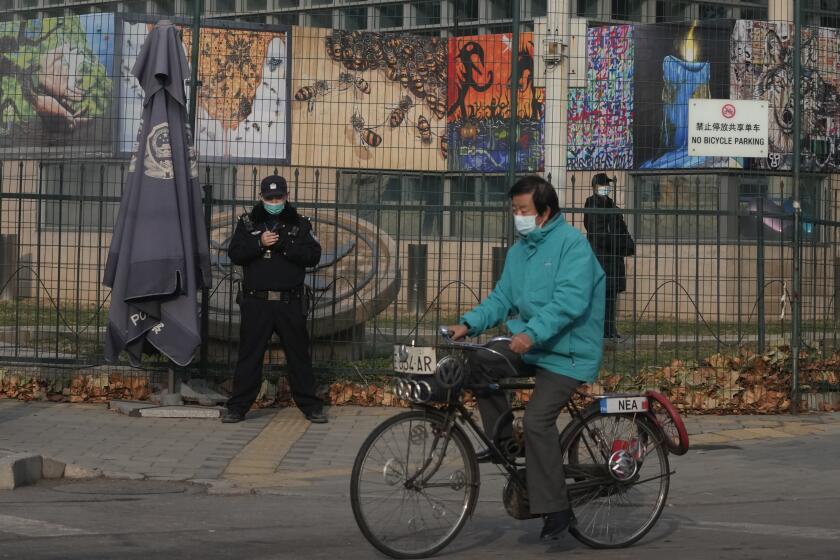 FILE - A resident on bicycle past by security personnel outside the U.S. Embassy in Beijing, China on Nov. 16, 2021. China and the U.S. have agreed to ease restrictions on each other's media workers amid a slight easing of tensions between the two sides. (AP Photo/Ng Han Guan, File)