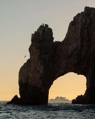 A boat is framed by the Arch of Cabo San Lucas as the sun sets.