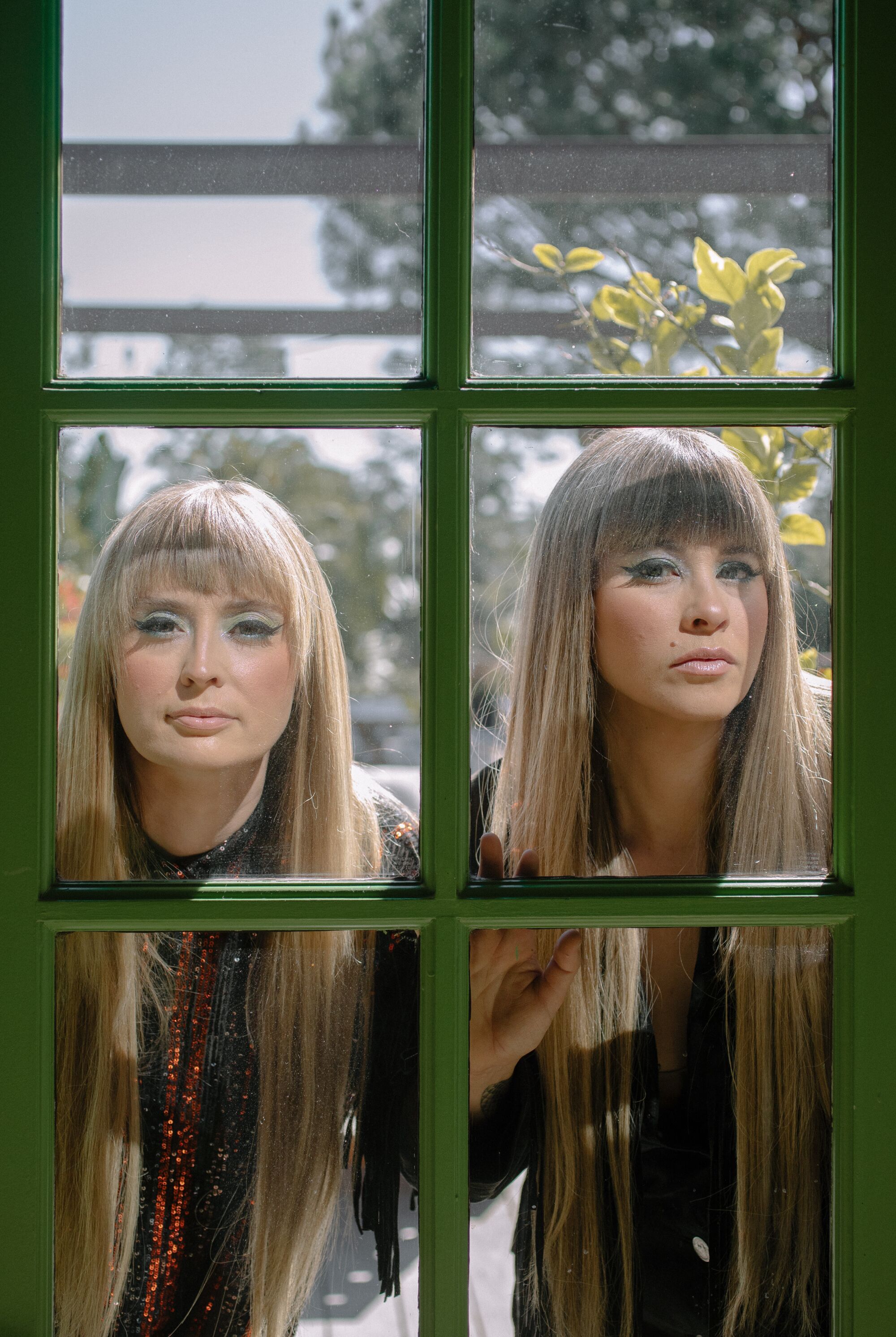 Two women with matching hair styles look through a window