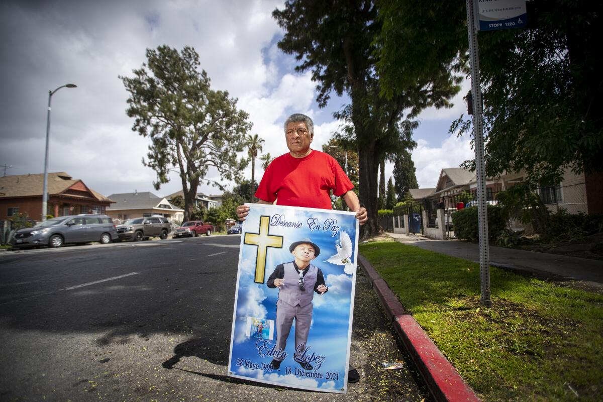 A man holds a memorial poster of his son on the street, where his son was fatally shot
