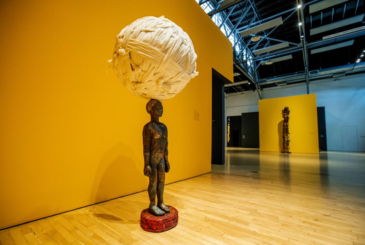 A figure of a woman balances an enormous ball of cloth on her head