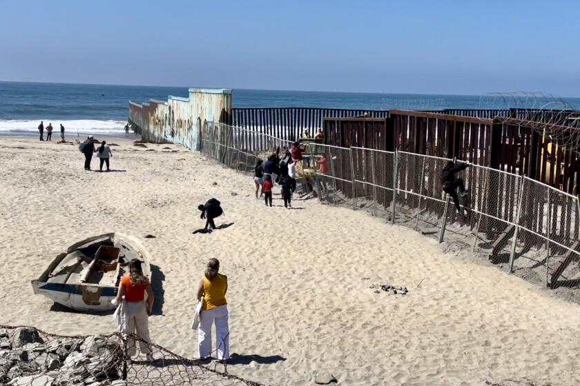 Un grupo de personas escala una cerca de alambre en la zona de construcción entre Playas de Tijuana e Imperial Beach el 26 de septiembre de 2023