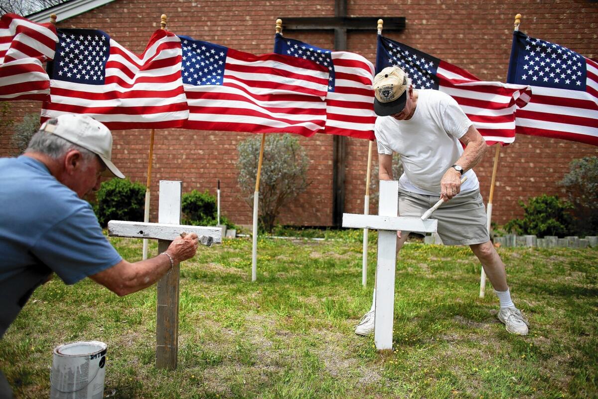 Bob Gordon, left, and Bob Butler paint crosses in front of 16 American flags as they build a memorial to the victims of the Ft. Hood shooting.
