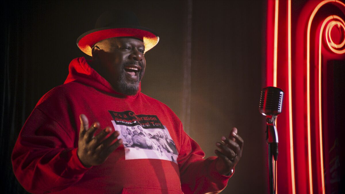 A man in a red sweatshirt and hat standing at a microphone onstage