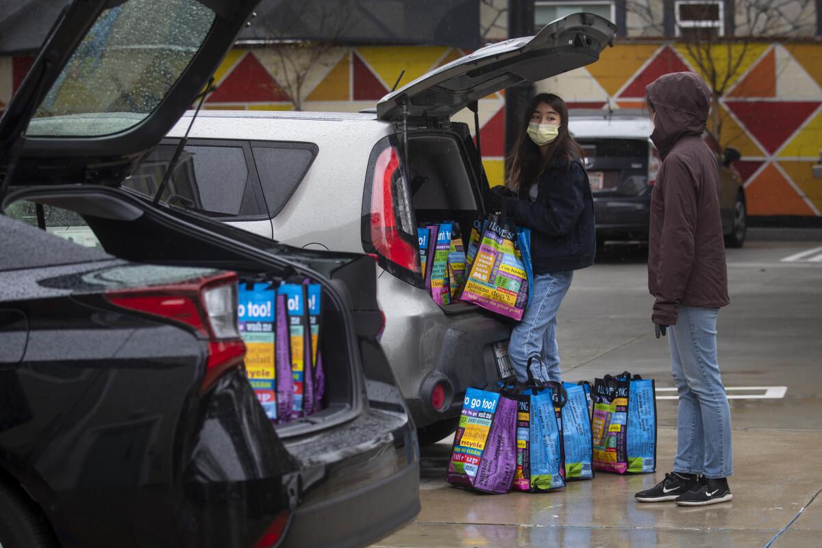 Volunteers Dylan Kim, left, and her mother Soo Kim load a car while helping deliver food to home-bound seniors in Hollywood on Thursday.