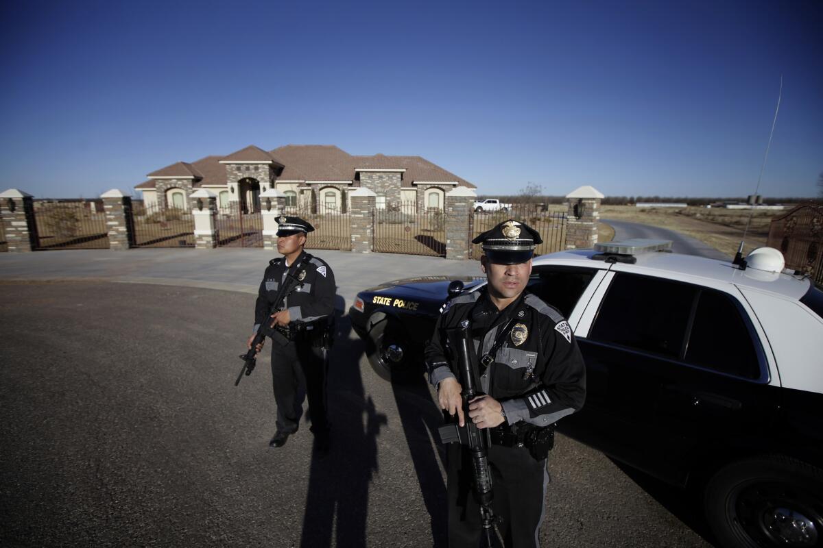 Two New Mexico State Police officers stand guard holding semiautomatic rifles outside the home of the alleged shooter at Berrendo Middle School in Roswell, N.M.