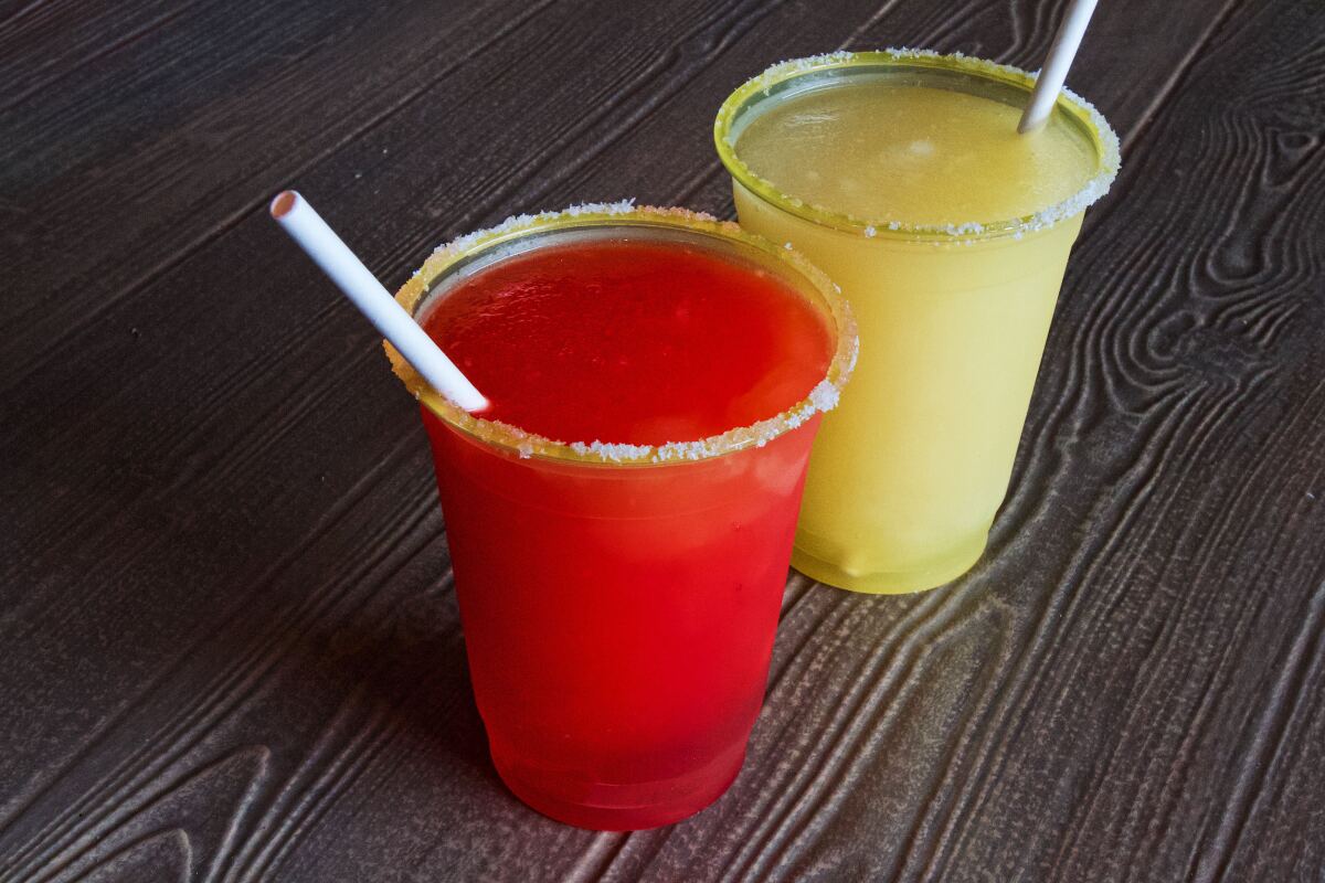 Two frozen, salt-rimmed margaritas in to-go cups: strawberry and lemon-lime
